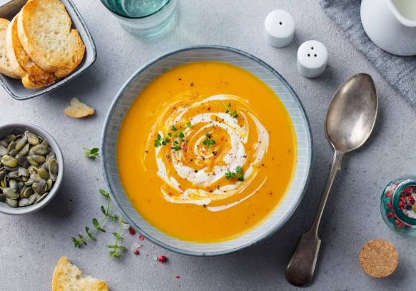 Pumpkin and carrot soup with cream on grey stone background. Top view