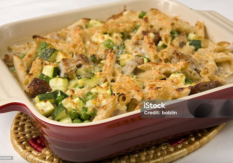 A gratin of pork containing roasted pork shoulder zucchini squash, peas, pasta, and topped with swiss Gruyere cheese.
