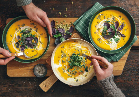 Men eating Vegan Creamy Roasted Pumpkin Soup on wooden background