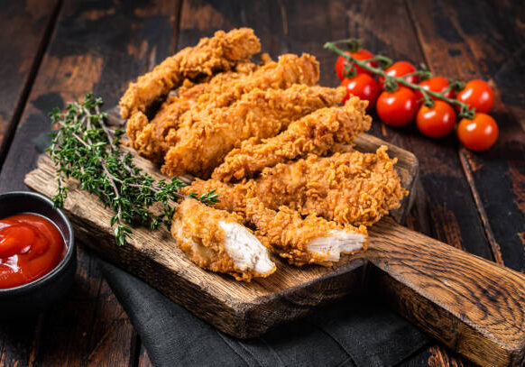 Crispy fried Breaded chicken strips, breast fillet meat with tomato ketchup on a plate. Wooden backgrund. Top view.