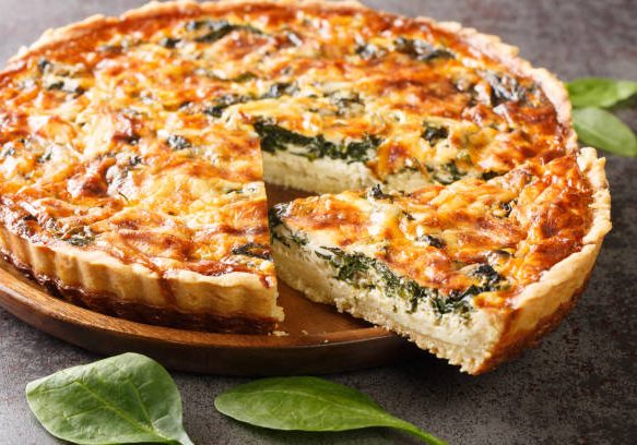 Quiche Florentine is a fresh spinach quiche baked in a homemade pie crust to serve for brunch or breakfast for dinner on gray table close-up. Hotizontal