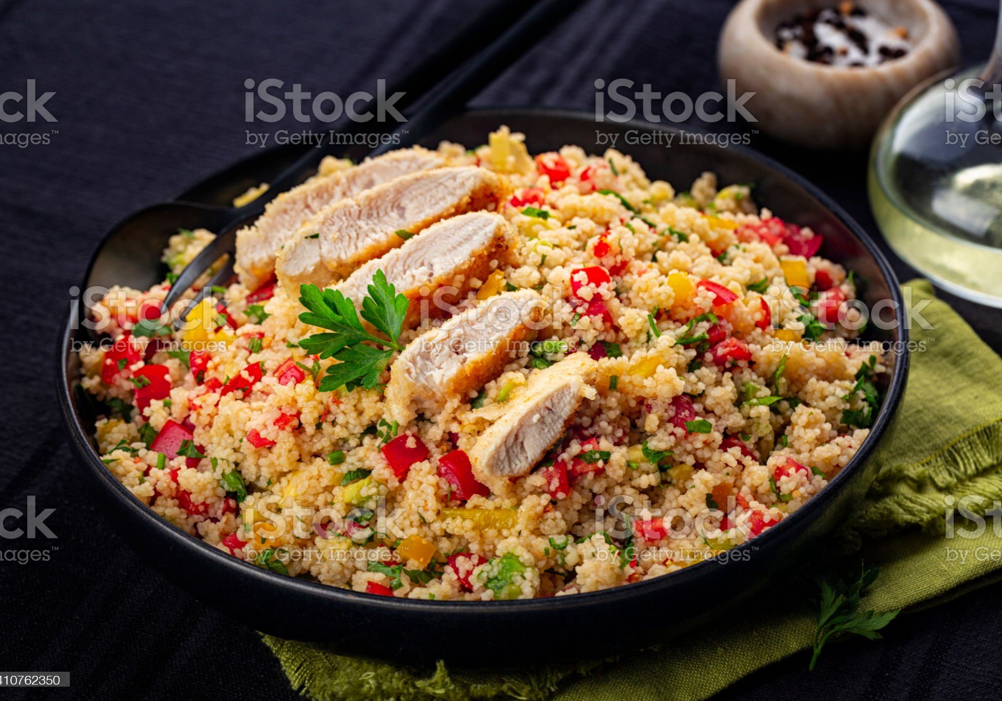 Couscous salad with Chicken breast and vegetables, tomatoes, avocado, bell pepper, parsley and lemon juice. Black table surface. Close-up.