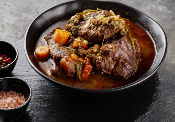 Traditional German braised beef cheeks in brown red wine sauce with herbs as closeup in black plate
