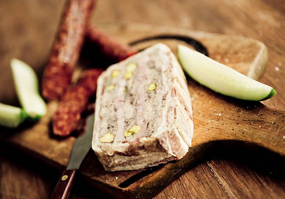 Rabbit and pistachio terrine wrapped with streaky bacon and served on an old wooden chopping board. Natural light.